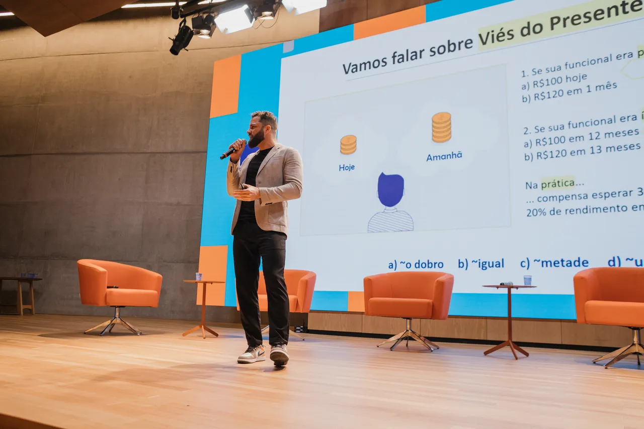 Philip Brás palestrando num palco de evento, com telão exibindo um slide sobre viés do presente